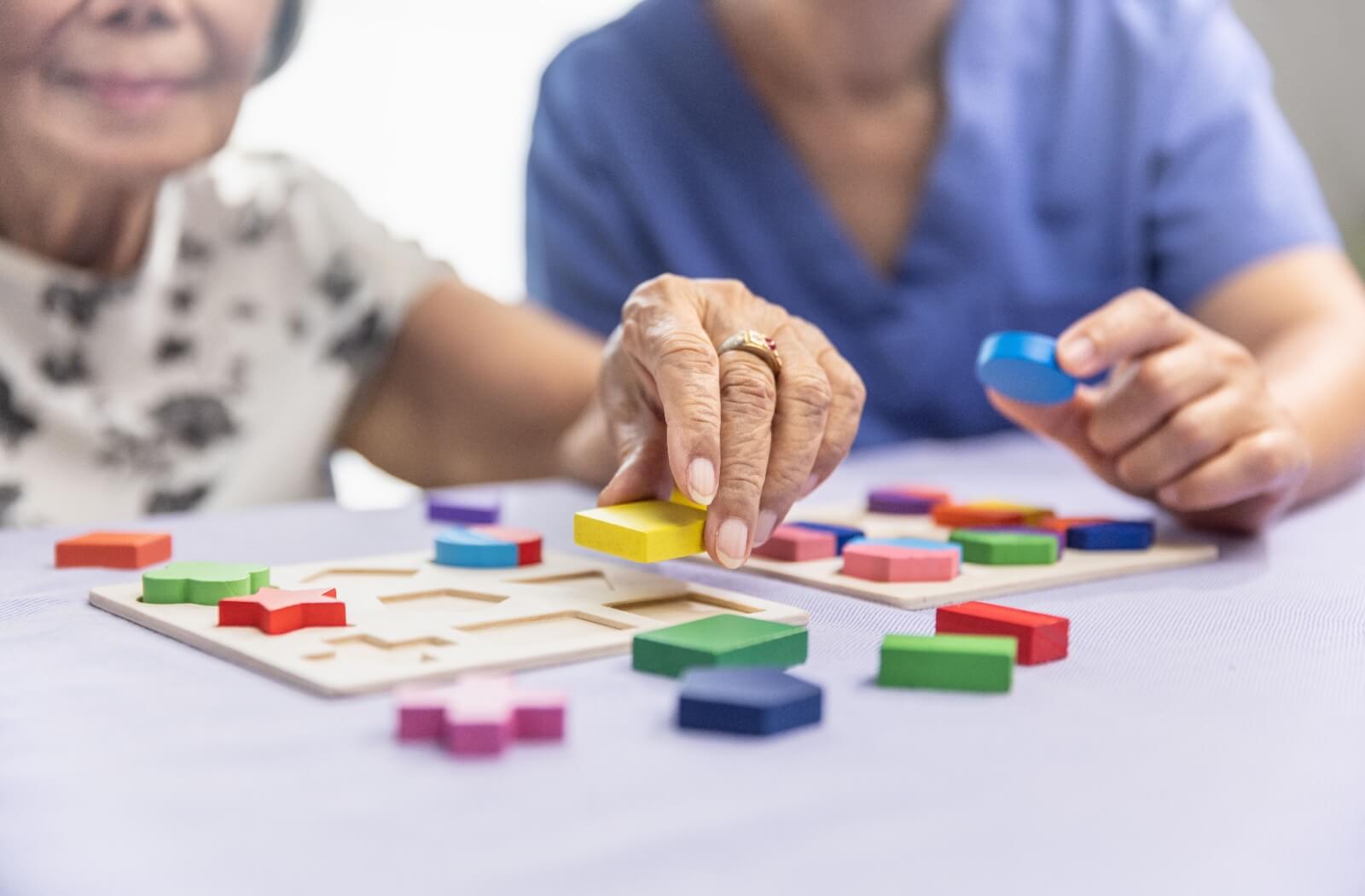 A caregiver and a senior woman engaging in a wooden shape puzzles game