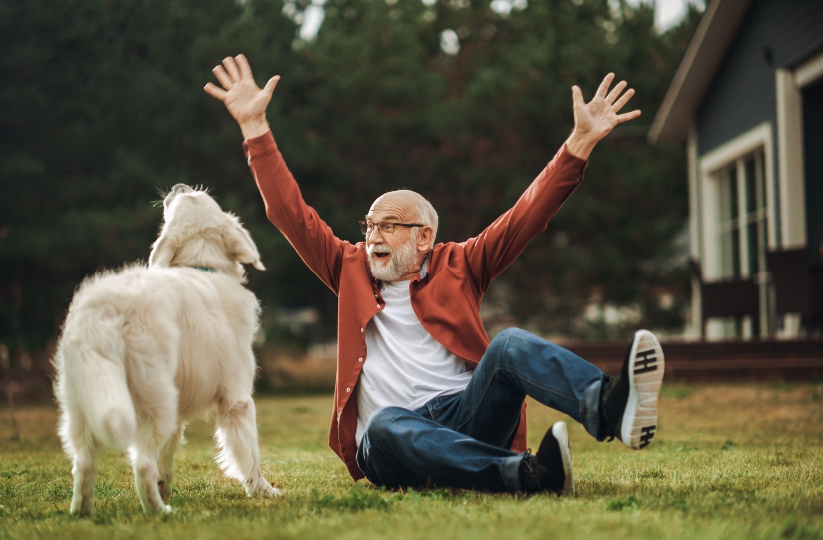 An older adult man plays with his dog on the lawn of an independent living community.