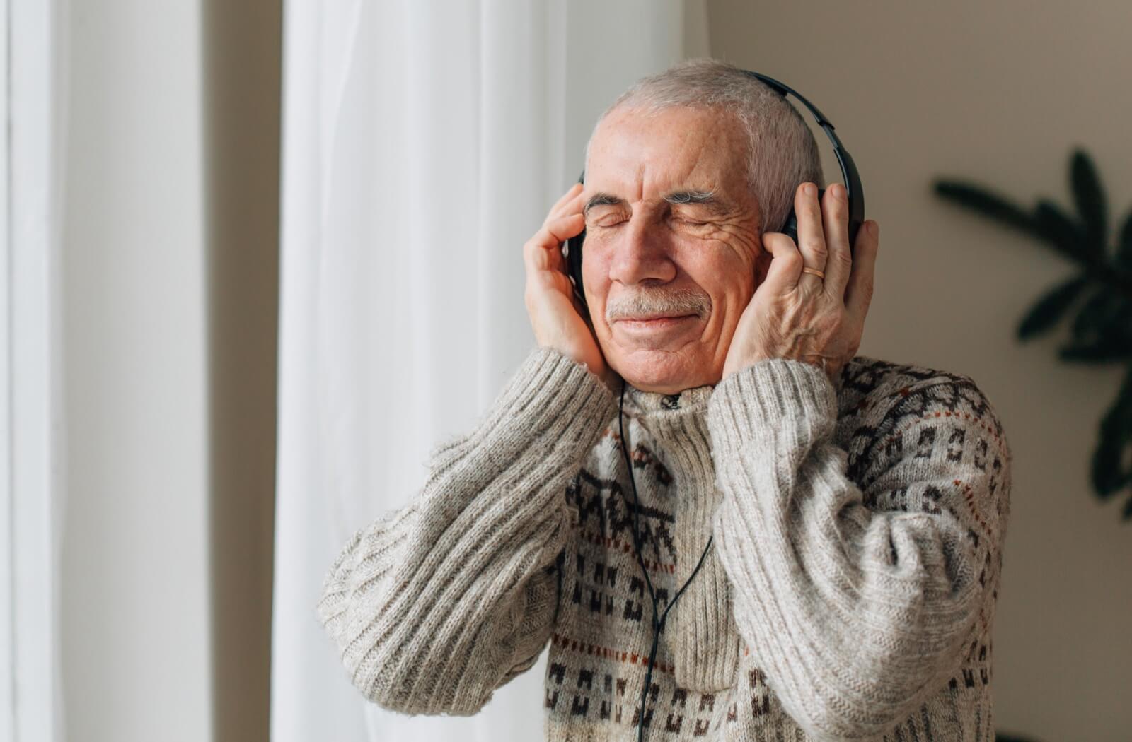 An older adult man closes his eyes and enjoys music therapy as part of dementia care.