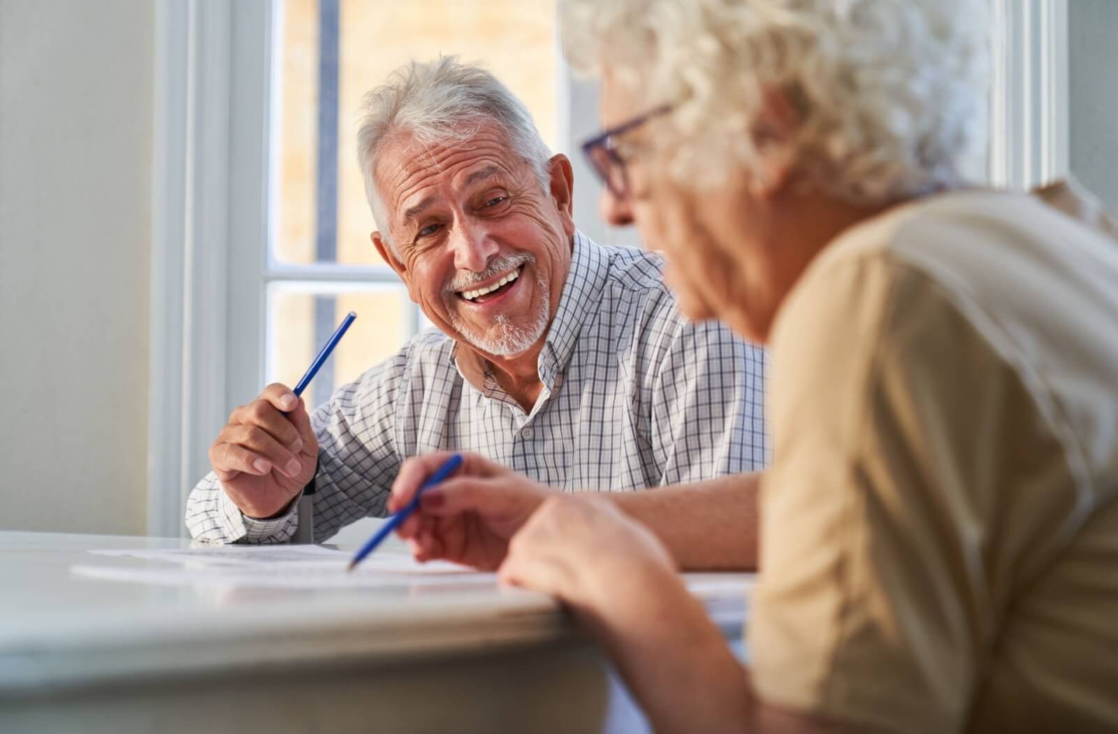 Two older adults smiling while doing memory puzzles together at a table in senior living.