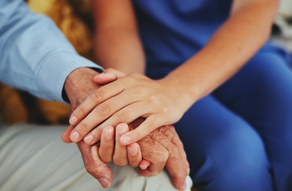 A close-up image of a caregiver holding the hand of an older adult to reassure them.