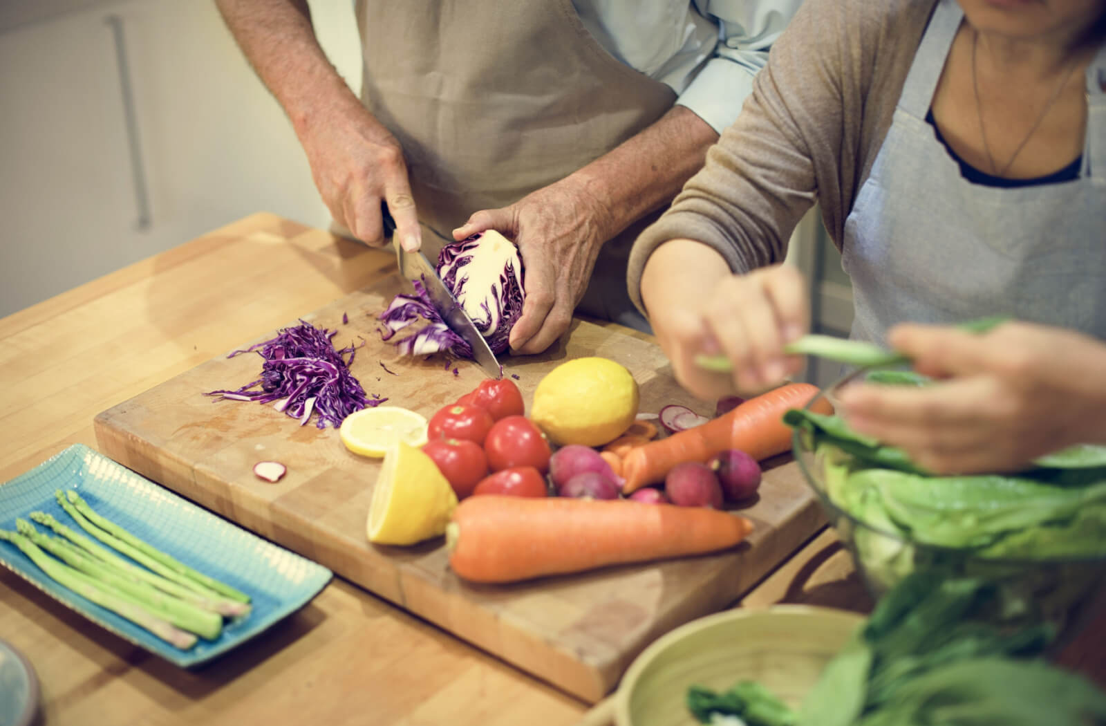 An older couple chops vegetables together for a nutritious salad