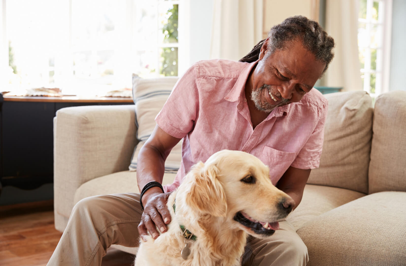 A happy senior man petting his pet dog in a sunlit room.