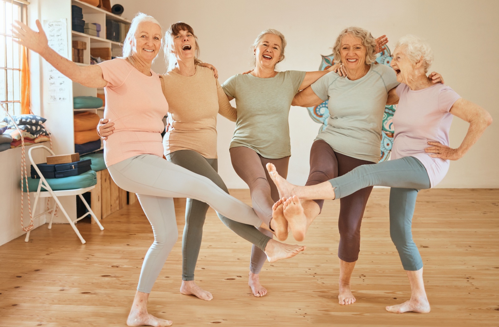 A group of older adult women laughing and balancing together in yoga class.