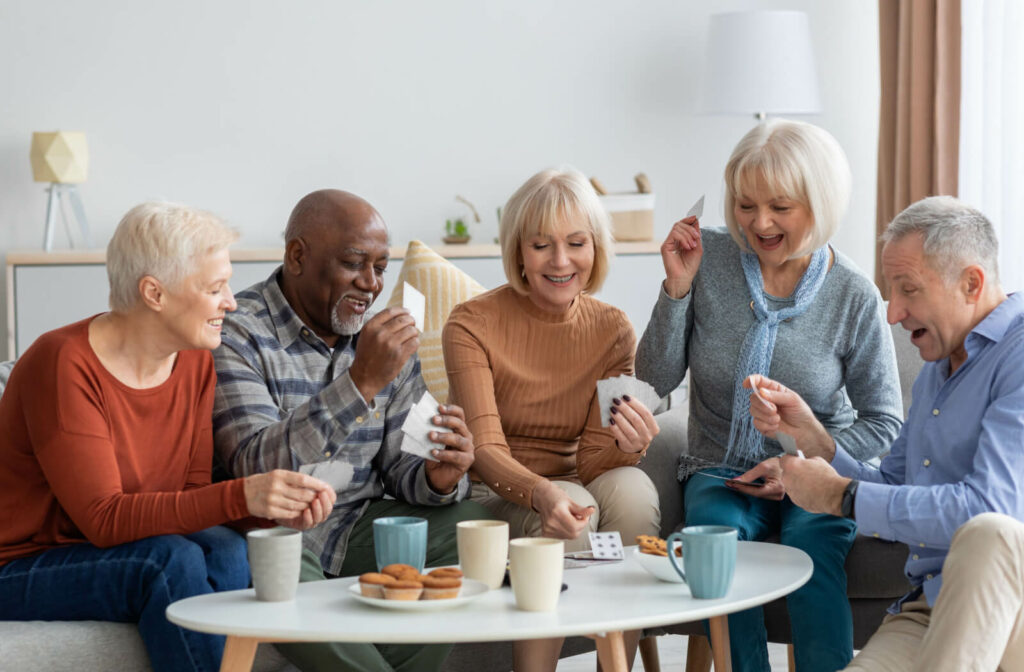 A group of seniors smiling, playing cards while sitting on a couch.