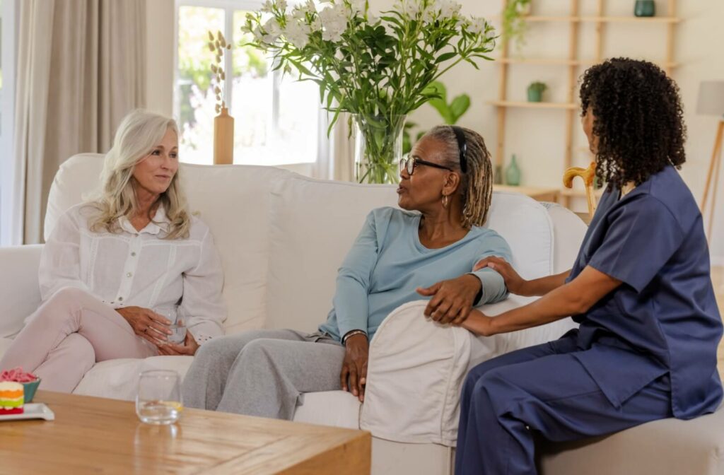 Older adult sitting on sofa with family member and care team member offering support in a bright living room